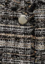 Conjunto de chaqueta y falda de tweed en tonos blanco, negro y dorado. La chaqueta es corta con cuello redondo, botones metálicos y bolsillos de parche. La falda es mini con abertura lateral y detalle de lazos.