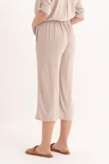 Conjunto de dos piezas color beige claro, compuesto por una camisa de manga corta con cuello y botones frontales, y un pantalón palazzo de tiro alto con detalle envolvente asimétrico en la parte delantera.