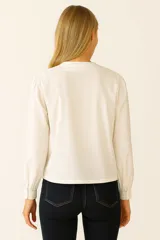 Blusa blanca con bordados florales en tonos celeste, rojo y marrón. Tiene cuello redondo con lazo ajustable y mangas largas abullonadas.