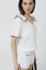 Blusa blanca de lino con cuello y mangas cortas con volados con borde de crochet marrón.