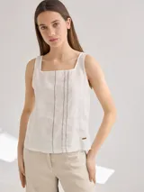 Musculosa blanca de lino con cuello cuadrado y tirantes anchos. Presenta tres líneas verticales de calados en el frente y un pequeño aplique de cuero con logo en el lateral. La espalda es de algodón con spandex.
