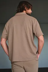 Camisa de manga corta color marrón claro, de punto texturizado de mezcla de algodón, con cuello abierto, tapeta lisa y bajo recto.