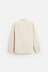 Camisa color crema de corte regular fit, confeccionada en tejido con viscosa. Tiene cuello solapa, manga larga con puños abotonados, bolsillo de parche en el pecho y cierre frontal con botones.