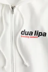 Campera blanca con capucha y cierre frontal, con bolsillos tipo canguro y puños acanalados. Estampado frontal con el logo de Dua Lipa y la frase "Training Season".
