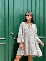 Vestido corto color gris claro, con escote en V, mangas 3/4 acampanadas, botones frontales y corte escalonado con volados.