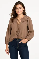 Camisa color crema con cuello a la base, mangas largas abullonadas con puños elásticos, escote en V con cordones y borlas.