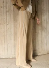Pantalón de vestir color beige, de corte recto y tiro medio, con cintura elástica y bolsillos laterales. Presenta una raya vertical blanca a lo largo de la pierna.