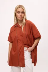 Camisa blanca de manga corta con cuello clásico, corte holgado y detalle de calado vertical en el frente.