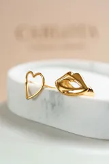 Par de aros asimétricos dorados de acero quirúrgico. Uno con forma de corazón y otro con forma de labios.