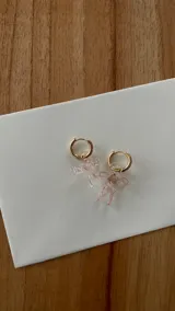 Par de aros colgantes con argollas de acero inoxidable y dijes de vidrio soplado con forma de moño, disponibles en color celeste y rosa.