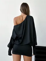 Vestido corto negro elastizado, asimétrico, de manga larga y hombro al descubierto.