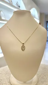 Collar dorado con dije ovalado de la Virgen María con borde de strass.