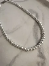 Collar corto de perlas blancas de plástico con cierre de mosquetón plateado.