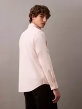 Camisa de manga larga color rosa claro, confeccionada en tejido Oxford de algodón y elastano. Presenta cuello camisero clásico, cierre frontal con botones y logo de Calvin Klein bordado en el pecho. Corte regular.