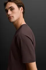 Camiseta deportiva marrón de tejido técnico ligero y elástico con estructura. Cuello redondo, manga corta, costuras planas y logo estampado.