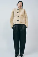 Chaqueta corta de cuello redondo y manga larga en tejido de pelo sintético color negro. Cierre frontal con botones metálicos dorados y bolsillos de plastrón. Colección Zara Woman.