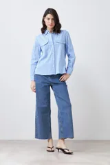 Camisa celeste con rayas verticales blancas, de manga larga y corte clásico, con cuello camisero y dos bolsillos con solapa en el pecho.