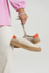 Zapatillas deportivas de cuero color beige con detalles en naranja y suela marrón.