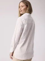 Camisa blanca de algodón con cuello clásico, cierre frontal con botones y mangas largas. Presenta bordados calados con motivos florales en la parte superior.
