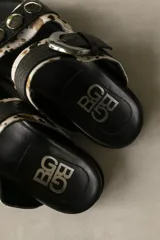 Sandalias bajas de cuero marrón con doble tira, hebilla ajustable y apliques de tachas metálicas.