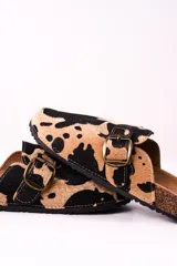 Zuecos con estampado de vaca en tonos camel y negro, con hebilla metálica ajustable y plantilla anatómica.