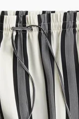 Pantalón amplio de tiro alto con cintura elástica y cordón de ajuste. Diseño a rayas verticales en blanco y negro.