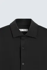 Camisa color beige de corte slim fit, confeccionada en tejido elástico que minimiza las arrugas. Tiene cuello italiano abierto, manga larga con puños abotonados y cierre frontal con botones.