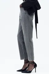 Pantalón de jean gris oscuro, de corte mom fit, tiro alto y largo tobillero. Cuenta con cinco bolsillos, cierre frontal con cremallera y botón.
