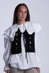 Chaleco tejido color crema con escote en V y cierre frontal con lazos. Presenta bordados de flores en tonos naranja, verde y blanco.