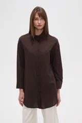 Camisa blanca de algodón con cuello clásico, corte holgado, cierre frontal con botones y mangas largas.