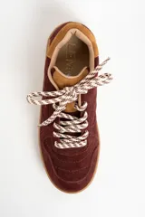 Zapatilla de cuero con capellada de gamuza en tonos borgoña y camel, con suela de goma color caramelo. Cordones trenzados en blanco y marrón.