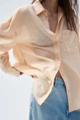 Camisa color durazno confeccionada en algodón, de corte amplio, con cuello solapa, manga larga con puños abotonados, hombros caídos, bolsillo de parche en el pecho, pinzas en la espalda y cierre frontal con botones.