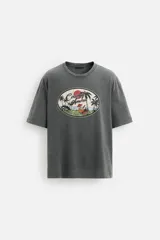 Camiseta gris de corte recto con cuello redondo y mangas cortas. Estampado ovalado con palmeras, sol y texto "Coconut Amora. Maui Offers Paradise".