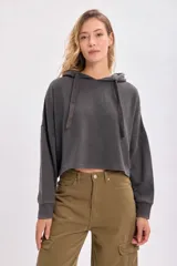 Canguro deportivo cropped gris oscuro con capucha y cordones ajustables. Corte holgado y mangas largas con puños ajustados.