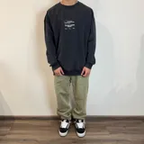 Buzo color crema de corte oversize con cuello redondo y puños acanalados. Presenta estampados en negro con motivos de palmeras, calamar, texto y logo de la marca.