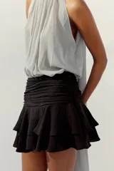 Falda pantalón corta de color negro, con tiro medio, detalle de pliegues en la cintura y volantes en el ruedo. Cierre lateral con cremallera.