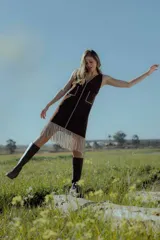 Vestido corto marrón de gamuza sintética, sin mangas, con escote en V y detalle de flecos en el ruedo. Presenta apliques bordados en el frente y laterales.