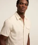 Camisa de hombre de manga corta confeccionada en una mezcla de lino y algodón, marca Marfinno. Presenta un calce confort, cuello clásico, cierre frontal con botones y un bolsillo de parche con solapa en el pecho. Las mangas cuentan con un detalle de dobladillo.