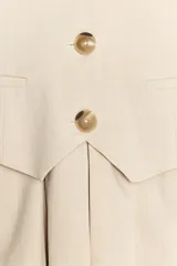 Vestido corto color beige, de escote pico y sin mangas. Tiene falsos bolsillos de vivo en el delantero, falda con tablas y detalle de trabilla en la espalda. Cierre lateral con cremallera oculta.