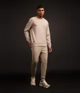 Conjunto deportivo color beige compuesto por un buzo de cuello redondo y un pantalón de jogging con cintura elástica y bolsillos laterales. El buzo es de corte clásico y el pantalón es ajustado en los tobillos.