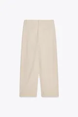 Pantalón color beige de tiro alto, corte ancho y largo midi, con pinzas delanteras, bolsillos laterales y traseros. Cierre frontal con cremallera y botón.