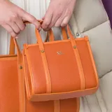 Cartera tote rectangular color naranja de cuero sintético graneado, con doble asa corta y correa larga regulable. Tiene cierre superior, dos bolsillos internos abiertos y uno con cierre.