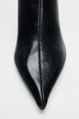 Botín negro de charol con punta fina, cierre de cremallera y tacón fino de 7 cm.