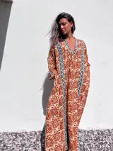 Túnica larga de color beige con estampado floral en tonos terracota y detalles geométricos en negro y blanco en el escote y a lo largo del frente.