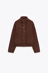 Chaqueta de punto marrón con cuello alto y manga larga. Tiene cierre frontal con botones y bolsillos de parche en el delantero.
