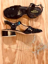 Sandalias de cuero charol negro con tiras anchas y hebilla al tobillo.