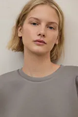 Buzo de tejido liso color gris, con cuello redondo y puños y ruedo ajustados.