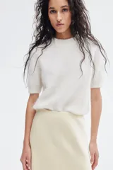 Pollera midi color crema, con leve brillo y caída suave. Modelo de tiro alto con elástico oculto en la cintura y leve vuelo en el bajo.