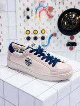 Zapatillas bajas de cuero color crema con detalles en azul marino y suela blanca. Presentan el logo de Star Wars en la lengüeta y el dibujo de R2-D2 en el lateral.