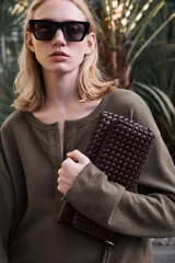 Bolso alargado color borgoña con diseño trenzado, asa bandolera y tirador con pulsera de mano. Incluye bolsillo interior, cierre mediante solapa y botón imantado.